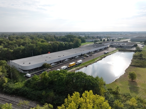 Aerial view of a long commercial warehouse building with a parking lot containing trucks and vans situated next to a pond and surrounded by trees in Indianapolis Indiana United States. Aerial view of a long commercial warehouse building with a parking lot containing trucks and vans situated next to a pond and surrounded by trees in Indianapolis Indiana United States.
