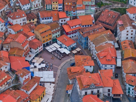 Aerial view of colorful houses with red tiled roofs surrounding a central plaza with people sitting at outdoor tables in Cudillero Asturias Spain. Aerial view of colorful houses with red tiled roofs surrounding a central plaza with people sitting at outdoor tables in Cudillero Asturias Spain.