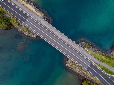 Aerial view of the bridge crossing Cudgen Creek with clear blue water rocky banks and lush green vegetation in Tweed Shire Council New South Wales Australia.