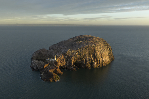 Aerial view of Bass Rock Lighthouse on the steep volcanic island surrounded by a gannet colony and calm sea at sunset North Berwick Scotland United Kingdom. Aerial view of Bass Rock Lighthouse on the steep volcanic island surrounded by a gannet colony and calm sea at sunset North Berwick Scotland United Kingdom.