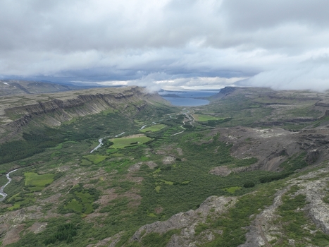 Aerial view of the lush green valley and winding river leading towards a distant fjord under a cloudy sky in Bifrost Borgarbyggd Iceland.