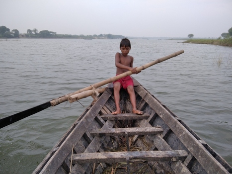 Kushtia Khulna Division Bangladesh 27 April 2020 View of a young boy rowing a wooden boat with a bamboo oar on the river with calm water and a hazy sky. Kushtia Khulna Division Bangladesh 27 April 2020 View of a young boy rowing a wooden boat with a bamboo oar on the river with calm water and a hazy sky.