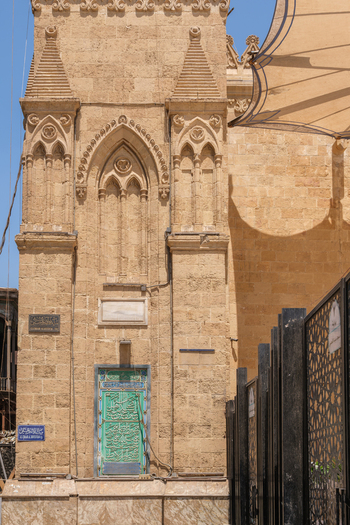 View of the Imam Al Hussein Mosque featuring intricate stone carvings a green door with Arabic calligraphy and a black geometric fence in Cairo Egypt. View of the Imam Al Hussein Mosque featuring intricate stone carvings a green door with Arabic calligraphy and a black geometric fence in Cairo Egypt.