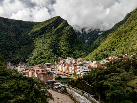 Aerial view of Aguas Calientes nestled in a lush green valley with a river flowing through the town surrounded by steep mountains in Aguas Calientes Cusco Peru.