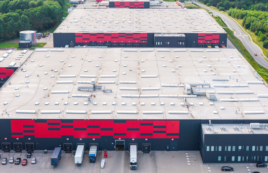 Aerial view of the large logistics warehouse facility with red and black facade loading docks and parked trucks in Kowale Pomeranian Voivodeship Poland. Aerial view of the large logistics warehouse facility with red and black facade loading docks and parked trucks in Kowale Pomeranian Voivodeship Poland.