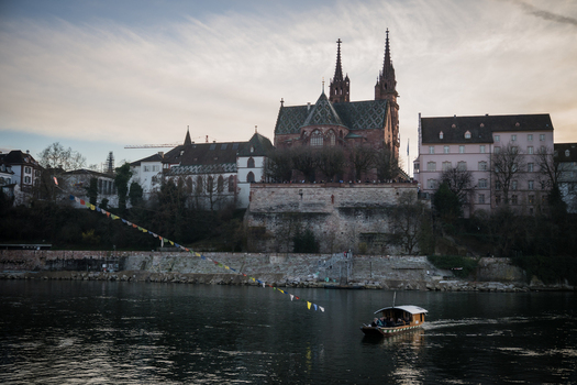 Basel Switzerland 10 March 2025 View of the majestic Basel Minster rising above the Rhine its spires piercing the dusk sky with a boat gliding along the water s surface. Basel Switzerland 10 March 2025 View of the majestic Basel Minster rising above the Rhine its spires piercing the dusk sky with a boat gliding along the water s surface.