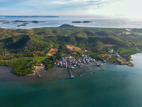 Aerial view of Galang Island featuring a traditional coastal village with wooden piers and fish farms along the shoreline Batam Riau Islands Indonesia.