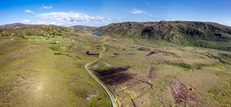 Aerial view of the rugged landscape of An Port featuring winding roads peat bogs and rolling hills under a clear blue sky in Ardara County Donegal Ireland.