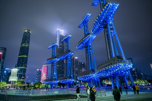 Guangzhou China 24 February 2024 View of illuminated blue sculptural structures in a modern urban square with skyscrapers and people walking at night. Guangzhou China 24 February 2024 View of illuminated blue sculptural structures in a modern urban square with skyscrapers and people walking at night.