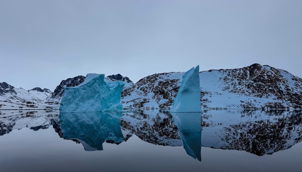 Aerial view of massive icebergs floating in calm fjord waters with snow covered mountains reflecting on the water at Tasiilaq Sermersooq Municipality Greenland. Aerial view of massive icebergs floating in calm fjord waters with snow covered mountains reflecting on the water at Tasiilaq Sermersooq Municipality Greenland.