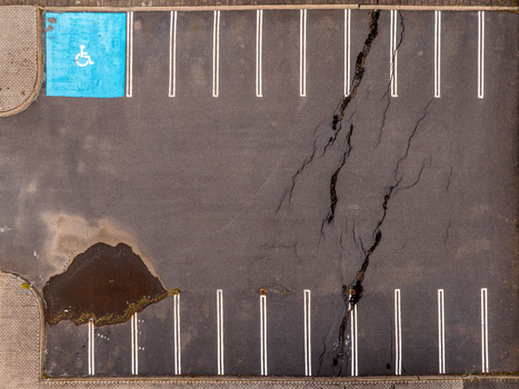 Aerial view of a cracked asphalt parking lot featuring a blue handicap parking space and a large puddle in Iceland. Aerial view of a cracked asphalt parking lot featuring a blue handicap parking space and a large puddle in Iceland.
