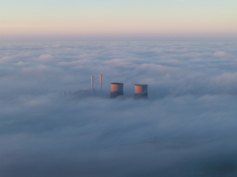 Aerial view of the RWE Clauscentrale power plant with cooling towers and chimneys emerging from a thick blanket of fog under a soft pastel sky in Maasbracht Limburg Netherlands. Aerial view of the RWE Clauscentrale power plant with cooling towers and chimneys emerging from a thick blanket of fog under a soft pastel sky in Maasbracht Limburg Netherlands.