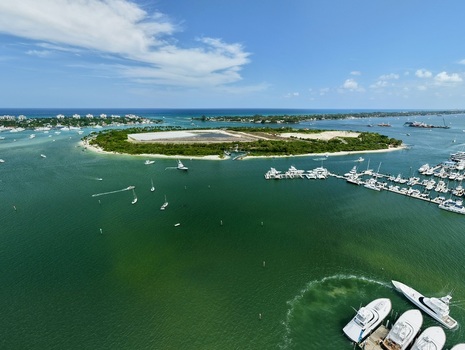 Aerial view of Peanut Island featuring lush vegetation white sand beaches and numerous boats anchored in the turquoise waters of the inlet Palm Beach County Florida United States.