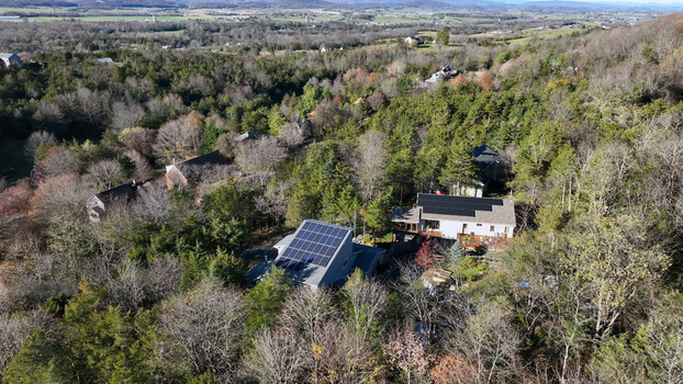 Aerial view of a modern house featuring rooftop solar panels nestled within a dense forest landscape in Harrisonburg Virginia United States.
