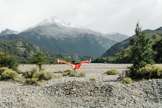 View of a person holding an orange wing in a rocky riverbed with snow capped mountains in the background in El Chalten Santa Cruz Province Argentina. View of a person holding an orange wing in a rocky riverbed with snow capped mountains in the background in El Chalten Santa Cruz Province Argentina.