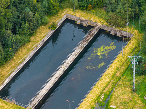Aerial view of a fish farming facility with two long rectangular concrete tanks filled with water surrounded by green trees and grass in Pomeranian Voivodeshi Poland. Aerial view of a fish farming facility with two long rectangular concrete tanks filled with water surrounded by green trees and grass in Pomeranian Voivodeshi Poland.