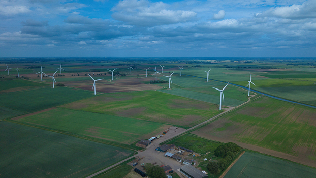 Aerial view of a wind farm with numerous turbines standing across green agricultural fields under a cloudy sky in March England United Kingdom.