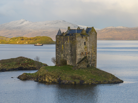 Aerial view of Castle Stalker on a small green island in Loch Laich with snow capped mountains in the background Appin Scotland United Kingdom. Aerial view of Castle Stalker on a small green island in Loch Laich with snow capped mountains in the background Appin Scotland United Kingdom.