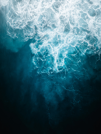 Aerial view of dark blue ocean with white foamy waves creating a dynamic contrast of light and shadow Noosa Heads Australia.