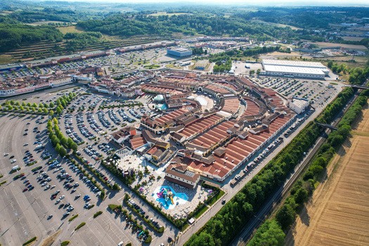 Aerial view of Designer Outlet Serravalle featuring red roofed shops extensive parking lots and a small water park in Serravalle Scrivia Piemonte Italy. Aerial view of Designer Outlet Serravalle featuring red roofed shops extensive parking lots and a small water park in Serravalle Scrivia Piemonte Italy.