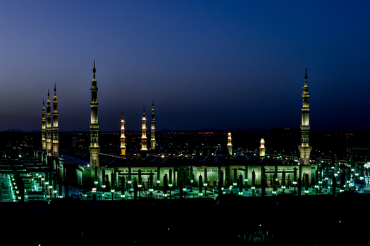 View of the illuminated Al Masjid e Nabawi at night with its towering minarets and glowing architecture in Madinah Al Madinah Province Saudi Arabia.