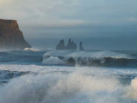 Aerial view of Reynisdrangar sea stacks rising from the turbulent Atlantic Ocean with crashing waves and dramatic coastal cliffs under a soft sky Myrdalshreppur Iceland. Aerial view of Reynisdrangar sea stacks rising from the turbulent Atlantic Ocean with crashing waves and dramatic coastal cliffs under a soft sky Myrdalshreppur Iceland.