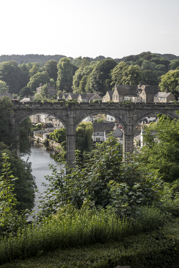 View of the historic stone arches of Knaresborough Viaduct spanning the River Nidd surrounded by lush green trees and traditional stone buildings in Knaresborough England United Kingdom.