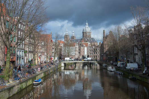 View of tranquil canal reflecting historic buildings under a moody sky lined with bicycles and bare trees Amsterdam North Holland Netherlands.