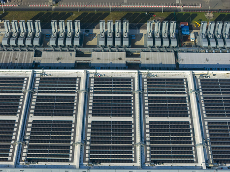 Aerial view of an AI data center with cooling towers and cloud computing hub exterior featuring solar panels on the roof. Aerial view of an AI data center with cooling towers and cloud computing hub exterior featuring solar panels on the roof.