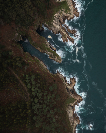 Aerial view of Xilloi Beach featuring rugged rocky cliffs crashing waves and dense green forest Vicedo Lugo Spain. Aerial view of Xilloi Beach featuring rugged rocky cliffs crashing waves and dense green forest Vicedo Lugo Spain.