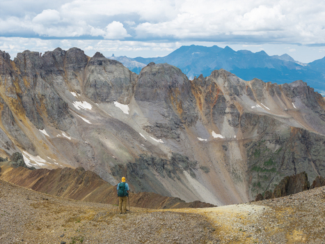 Aerial view of a hiker standing on a ridge overlooking the rugged Yankee Boy Basin and the towering peaks of Mount Sneffels in the San Juan Mountain Range Ouray Colorado United States. Aerial view of a hiker standing on a ridge overlooking the rugged Yankee Boy Basin and the towering peaks of Mount Sneffels in the San Juan Mountain Range Ouray Colorado United States.