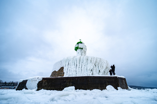 View of the frozen Molenfeuer Sassnitz lighthouse covered in thick ice with people taking photographs on a cold winter day in Sassnitz Mecklenburg Vorpommern Germany.