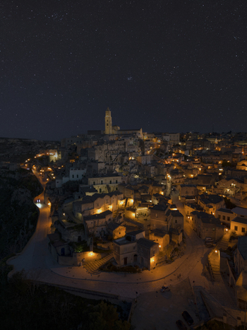 View of illuminated medieval architecture under a starry sky at twilight Matera Italy.
