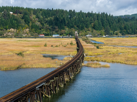 Aerial view of railroad tracks crossing marsh and open water near Florence Oregon highlighting the man made rail route through a quiet coastal wetland landscape.