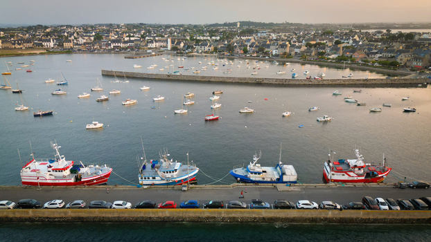 Aerial view of boats bobbing gently in the harbor contrasting with the rigid lines of parked cars framed by the quaint town of Roscoff Brittany France.