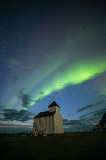 View of a small white wooden church under the vibrant green aurora borealis in the night sky in Leknes Lofoten Norway.