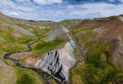 Aerial view of Grensdalur valley featuring a winding river cutting through vibrant green hills rugged volcanic slopes and rocky terrain in Sveitarfelagid Olfus Iceland. Aerial view of Grensdalur valley featuring a winding river cutting through vibrant green hills rugged volcanic slopes and rocky terrain in Sveitarfelagid Olfus Iceland.