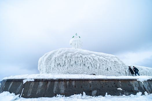 View of the frozen Molenfeuer Sassnitz lighthouse covered in thick ice with people standing nearby on the pier in Sassnitz Mecklenburg Vorpommern Germany.