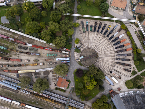 Aerial view of the Hungarian Railway Museum featuring a historic roundhouse with steam locomotives arranged on tracks surrounded by lush trees and greenery in Budapest Hungary. Aerial view of the Hungarian Railway Museum featuring a historic roundhouse with steam locomotives arranged on tracks surrounded by lush trees and greenery in Budapest Hungary.