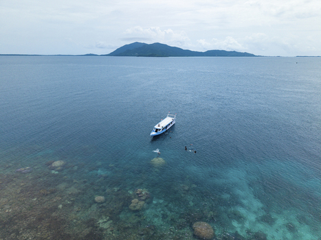 Aerial view of a pristine turquoise sea with a boat anchored near the vibrant coral reefs Cemara Kecil Snorkeling Spot Karimunjawa Central Java Indonesia.