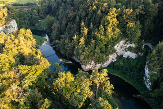 Aerial view of Teufelsbrucke bridge and the Danube river winding through dense green forests and limestone rock formations during golden hour in Inzigkofen Baden Wurttemberg Germany. Aerial view of Teufelsbrucke bridge and the Danube river winding through dense green forests and limestone rock formations during golden hour in Inzigkofen Baden Wurttemberg Germany.