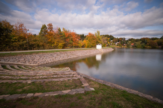 View of Velka Richnava lake with stone paved embankments and autumn foliage under a cloudy sky in Stiavnicke Bane Banska Bystrica Region Slovakia.