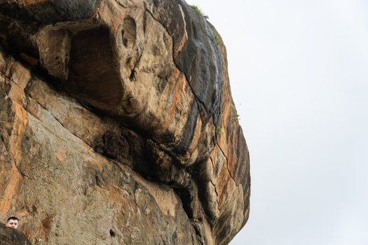 View of the massive weathered rock face of Sigiriya Rock with mineral streaks and a person visible at the bottom in Sigiriya Central Province Sri Lanka. View of the massive weathered rock face of Sigiriya Rock with mineral streaks and a person visible at the bottom in Sigiriya Central Province Sri Lanka.