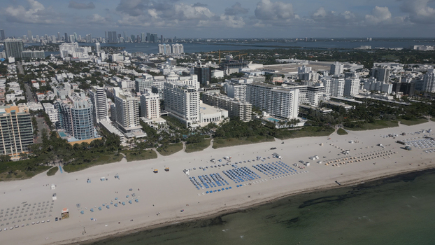 Aerial view of Miami Beach featuring white sandy shores rows of beach umbrellas and high rise hotels along the coastline in Miami Beach Florida United States. Aerial view of Miami Beach featuring white sandy shores rows of beach umbrellas and high rise hotels along the coastline in Miami Beach Florida United States.