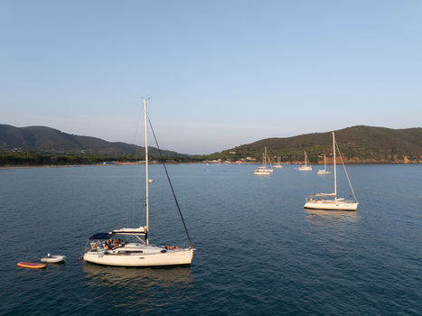 Aerial view of sailboats anchored in the calm blue waters of Lacona Bay with lush green hills in the background in Lacona Tuscany Italy.