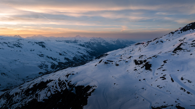 Aerial view of a pristine snow blanketed mountain range under a pastel sky the slopes bathed in the soft light of dawn Val Thorens Auvergne Rh&ocirc;ne Alpes France.