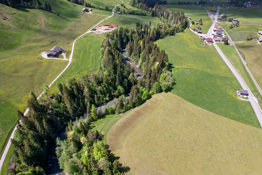 Aerial view of a river winding through a lush valley with dense pine forests green meadows and scattered chalets in Rougemont Vaud Switzerland. Aerial view of a river winding through a lush valley with dense pine forests green meadows and scattered chalets in Rougemont Vaud Switzerland.