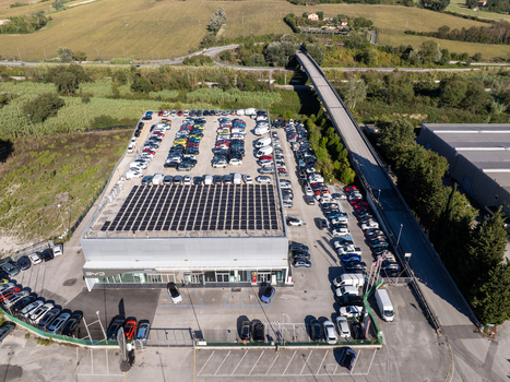 Aerial view of a car dealership featuring a large parking lot filled with vehicles and a roof covered in solar panels situated near a highway overpass in Ancona Marche Italy. Aerial view of a car dealership featuring a large parking lot filled with vehicles and a roof covered in solar panels situated near a highway overpass in Ancona Marche Italy.