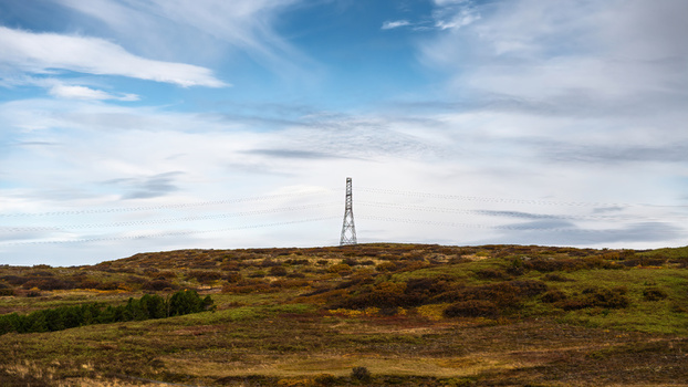View of high voltage power lines standing on a grassy hill under a cloudy sky in Iceland.