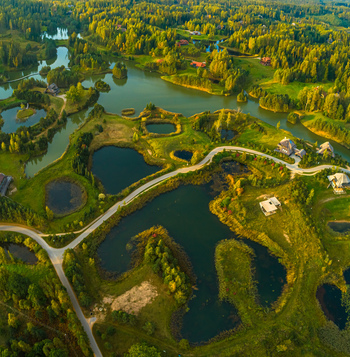Aerial view of a lush green landscape featuring interconnected lakes winding roads and scattered houses in Latvia. Aerial view of a lush green landscape featuring interconnected lakes winding roads and scattered houses in Latvia.